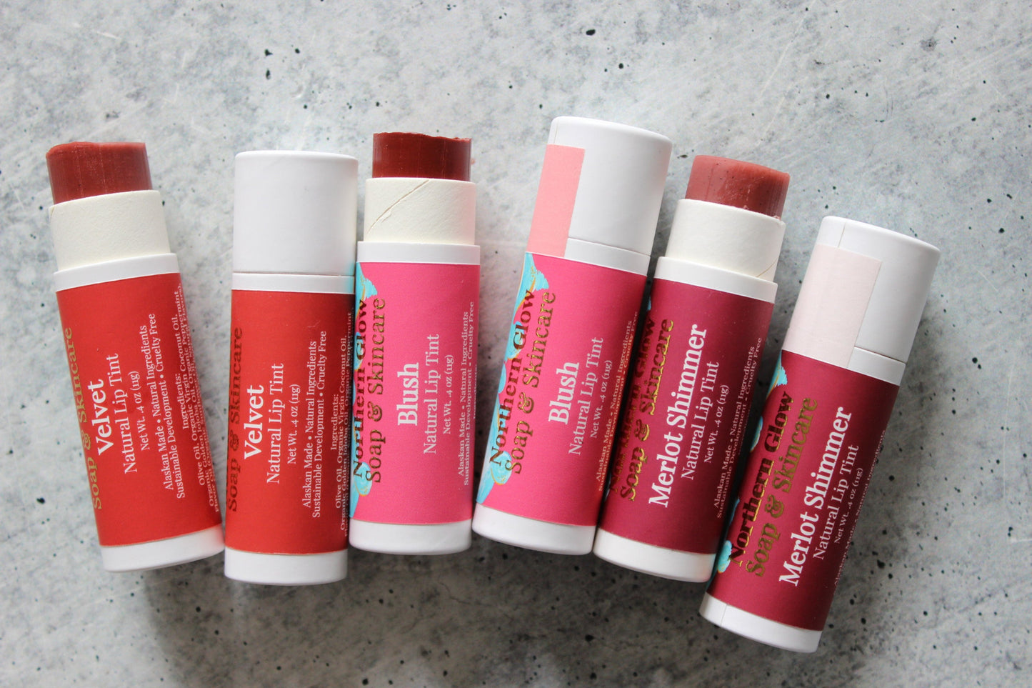 Set of lip balm sticks with visible branding on a gray surface