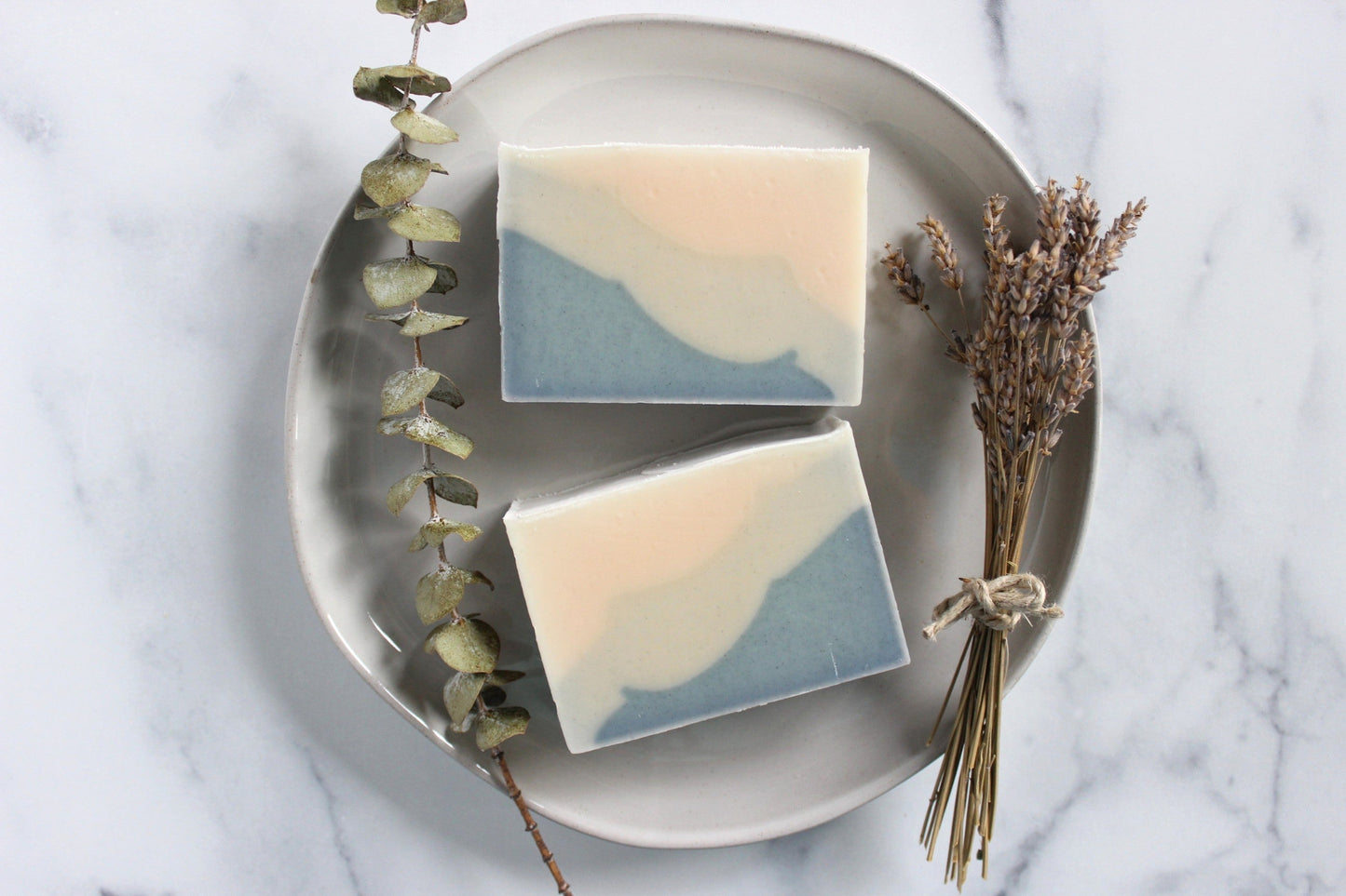 A plate with two Ocean Goddess soaps next to dried lavender and eucalyptus sprigs.