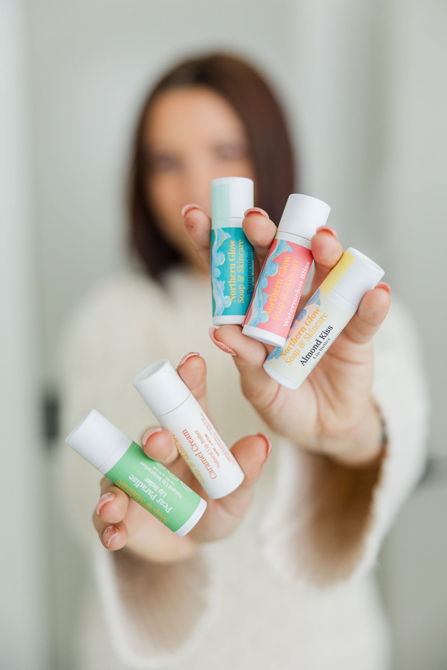 Person holding five tubes of different lip balms with a blurred background