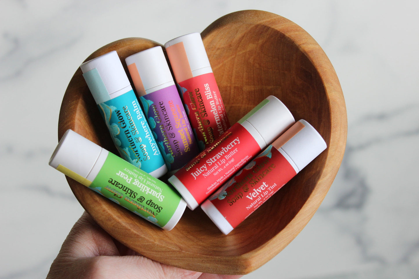 Assorted lip balms in a wooden heart-shaped bowl on a marble surface