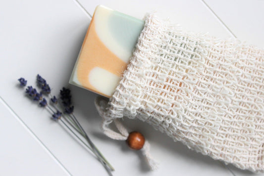 Cambric soap saver pouch with green, orange and white soap slipping out of bag.  Dried lavender in background.