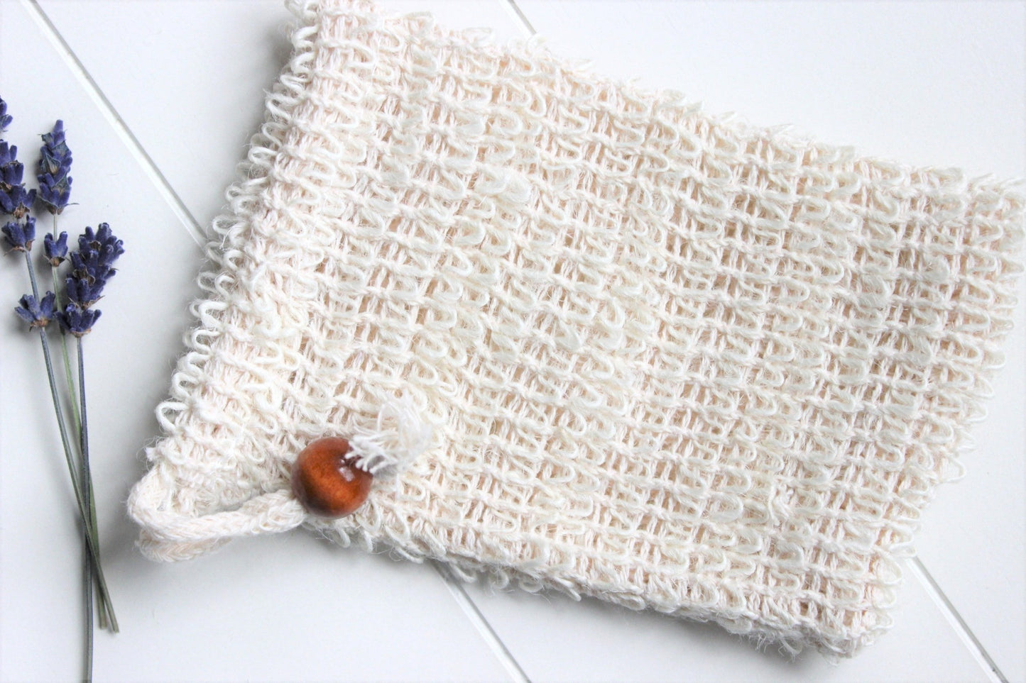A cambric soap saver with a wooden bead. Dried lavender in background.