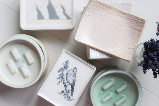 Ceramic soap dish stacked together.  Some with mountains, wood grain, circular dishes, dishes with birds.