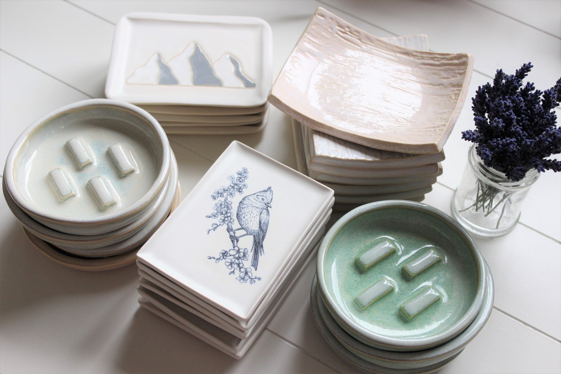 Handmade ceramic soap dishes stacked in piles.  Circular dishes, rectangular dishes and some with birds.