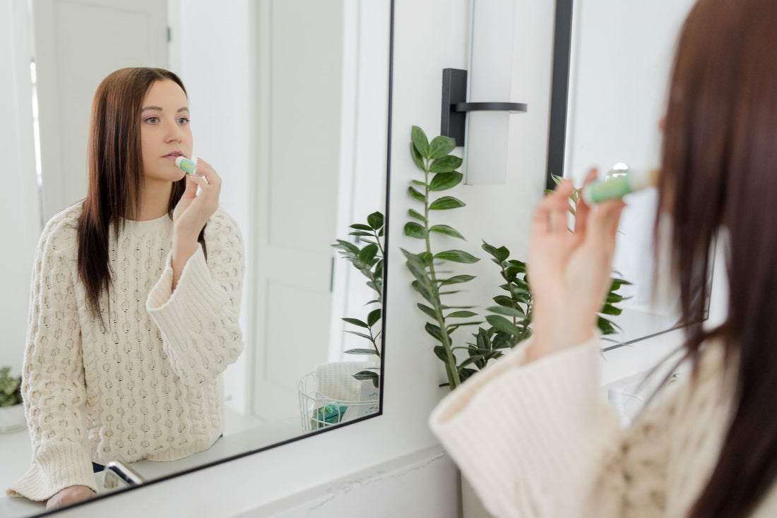 Woman in mirror applying Northern Glow Soap and Skincare's lip balm.