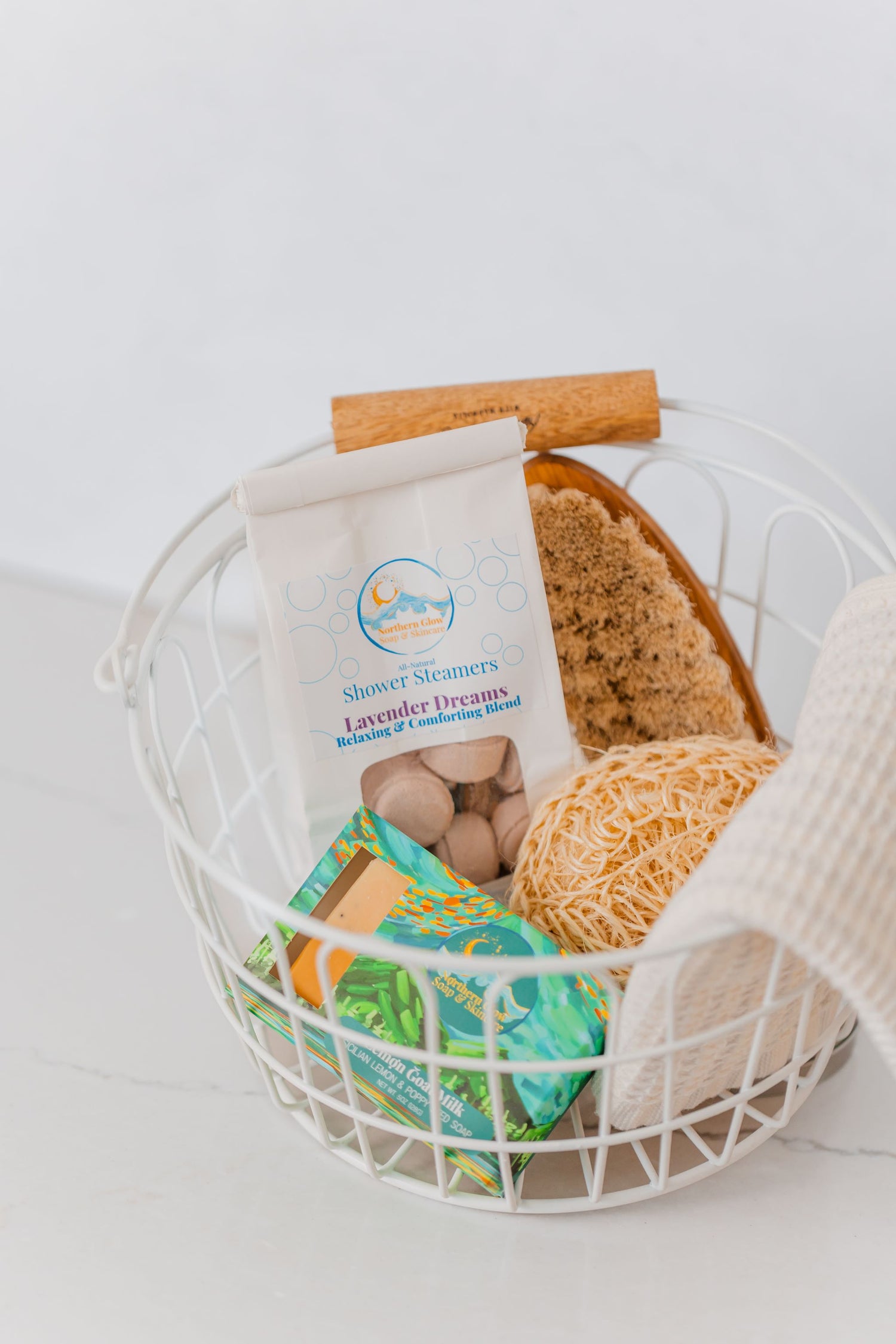 A basket is full of shower steamers, Alaska made soaps, a washcloth, and brushes.