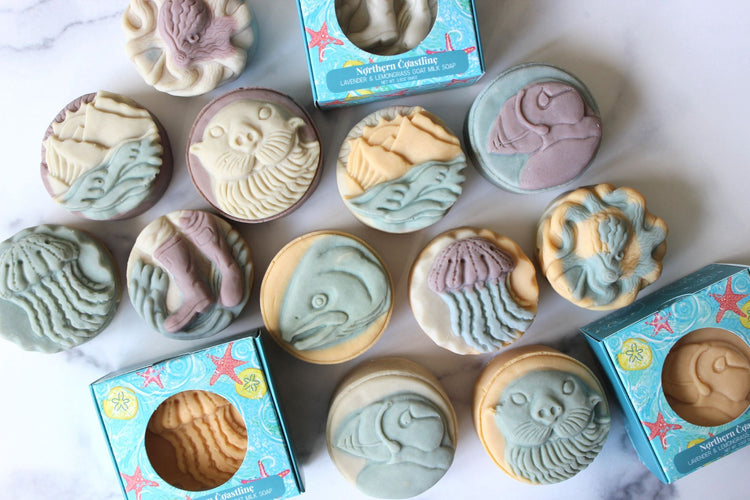 Kachemak Bay bar soaps shaped like otters, puffins, salmon and seashells are in white boxes.