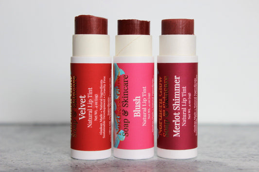 Three lip balm sticks with red and white packaging on a gray surface.