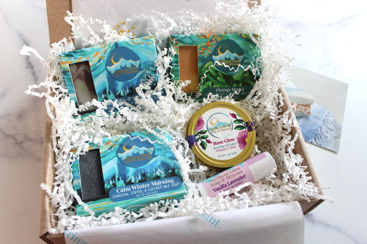 Gift box with bath and body products including soaps and skincare on a marble surface.