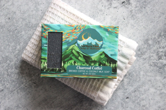 Charcoal coffee soap in a green box, on a white washcloth.