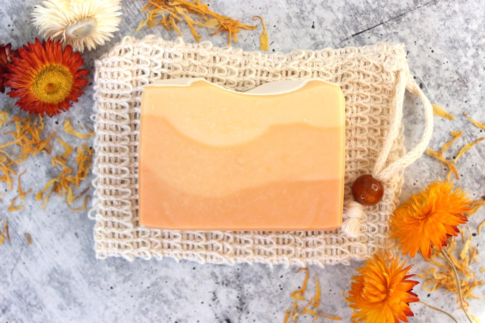 Coconut milk soap with red Brazilian clay next to red and orange flowers.