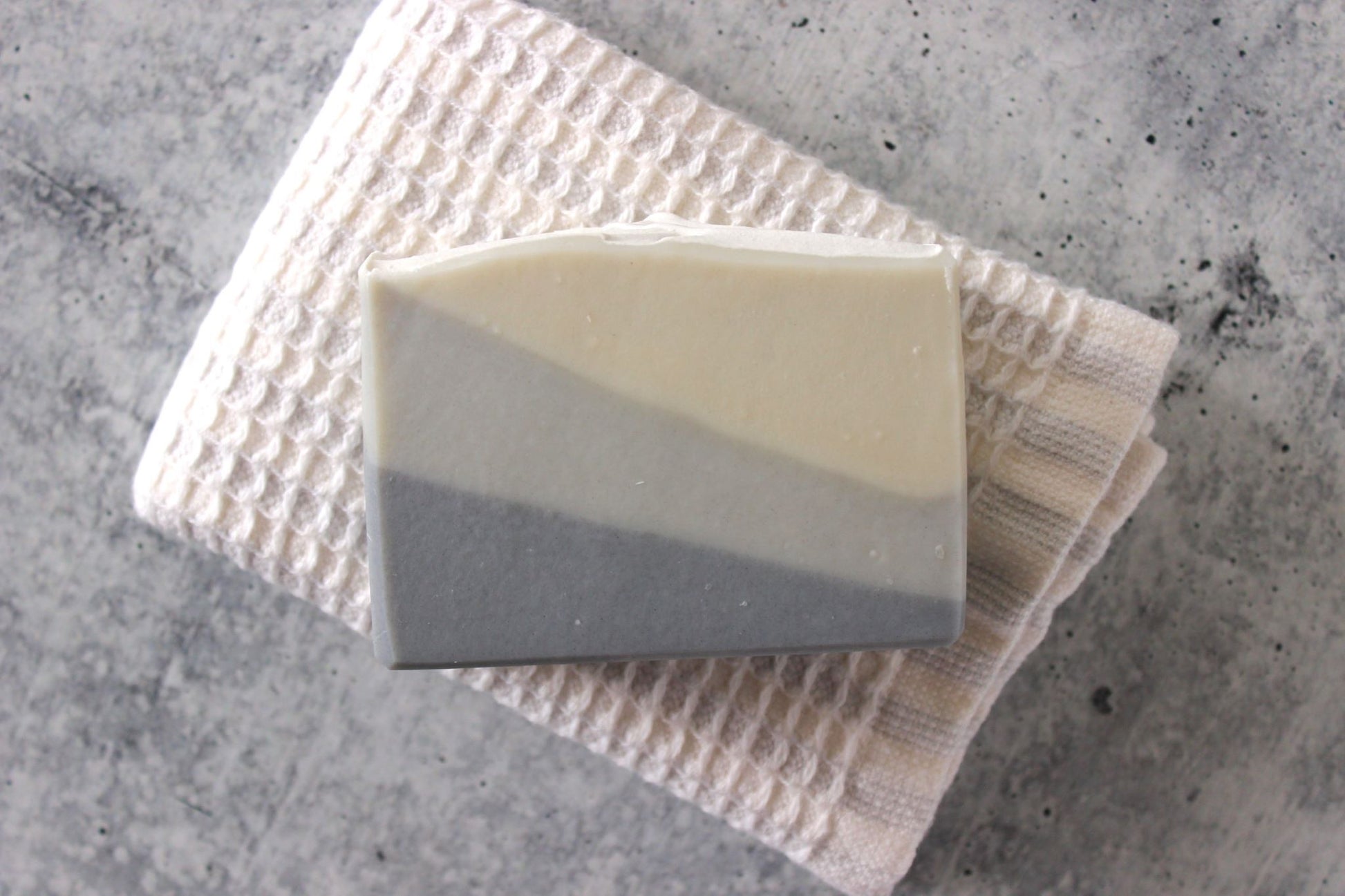 Three-layered soap bar on a textured towel with a concrete background