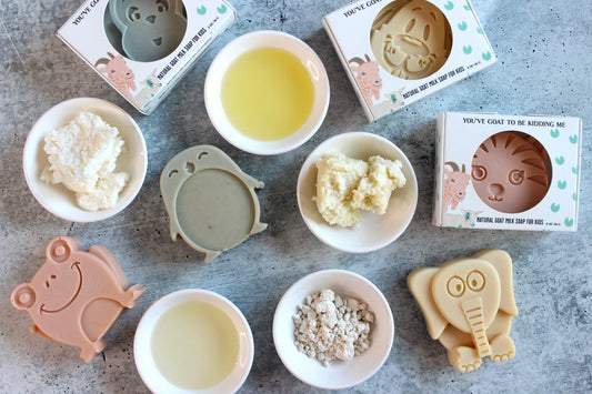 Goat milk soap for kids in white boxes, surrounded by natural ingredients in white bowls.