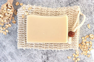 Goat milk soap for sensitive skin. Oatmeal and a wooden scoop are spread around the soap bar.