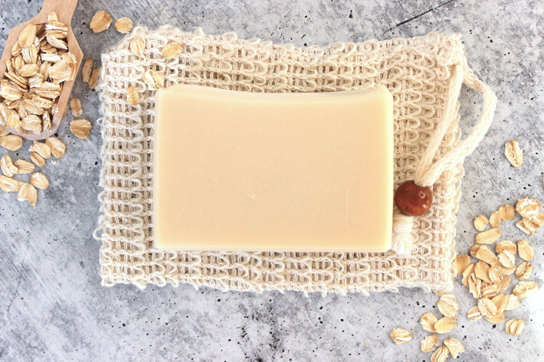 Goat milk soap for sensitive skin. Oatmeal and a wooden scoop are spread around the soap bar.