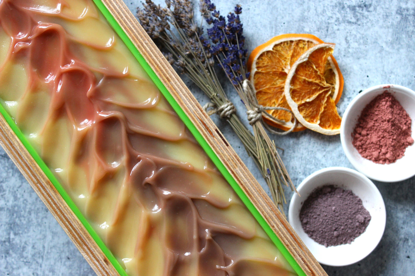 Lavender body soap in a wooden mold next to dried lavender and natural clays.