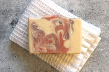 Load image into Gallery viewer, Lavender goat milk soap with pink and purple swirls, on a white washcloth.
