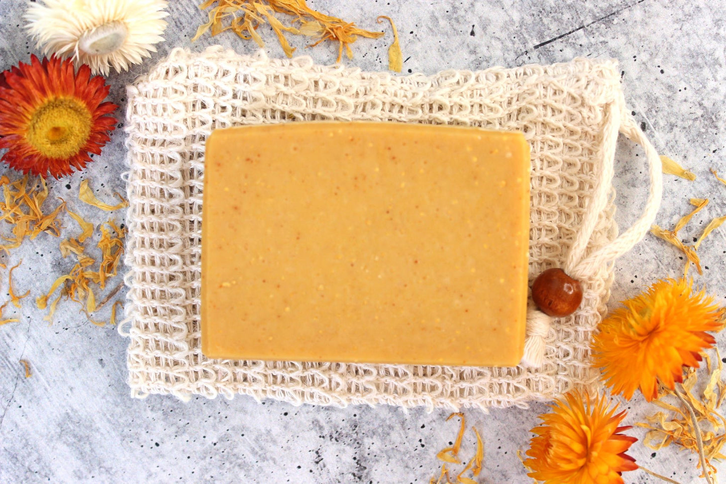 Golden yellow turmeric soap on a white soap saver bag. Dried floral all around.
