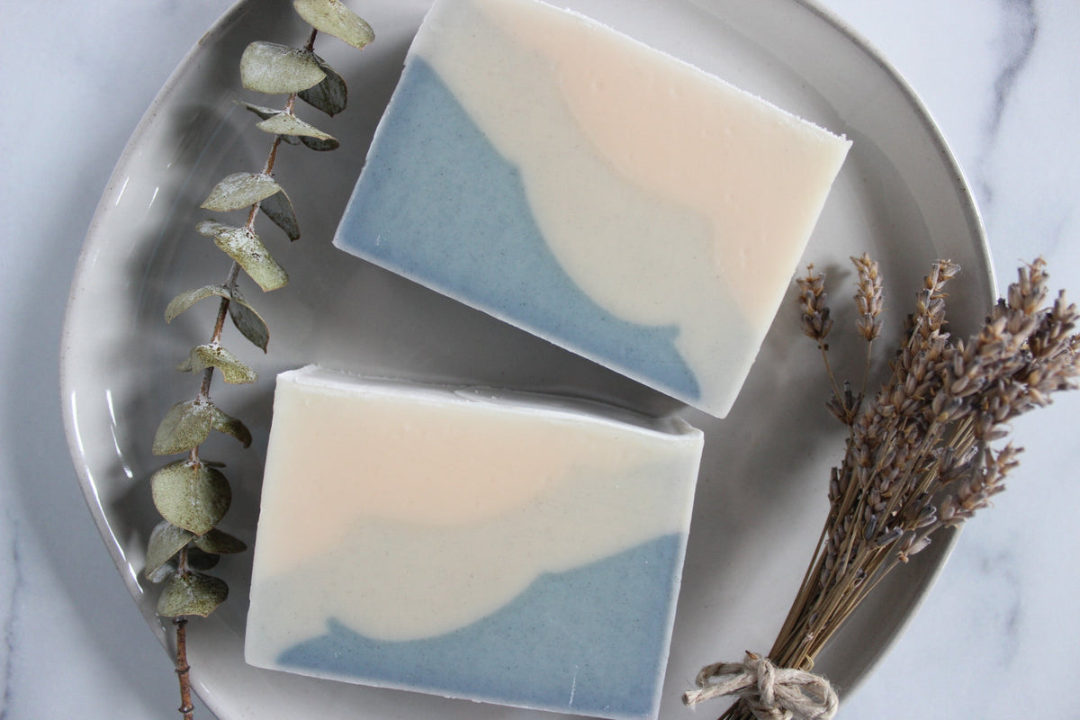 Two bars of Alaska sea kelp soap sit next to dried eucalyptus and lavender, on a gray round plate.
