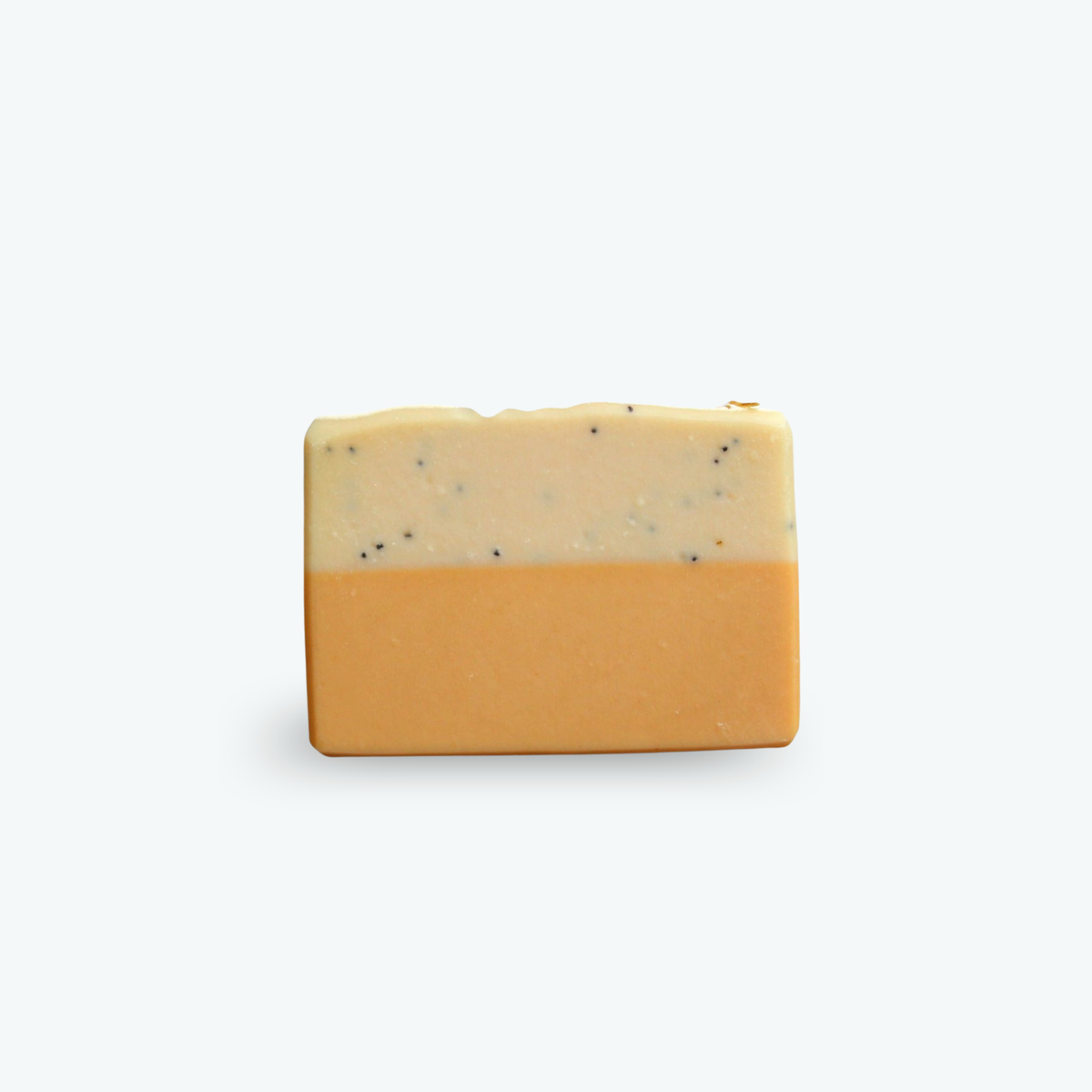 A rectangular bar of handmade soap with a two-tone design, featuring a solid yellow bottom half and a cream-colored top half speckled with small black seeds, set against a plain light gray background.