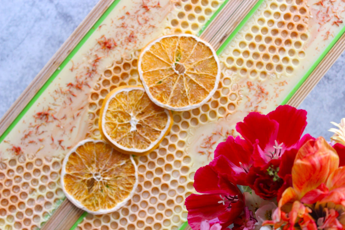 Skin-loving orange and Alaska Honey soap in wooden soap molds. Pictured next to dried oranges and flowers.