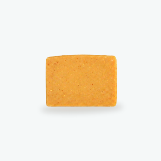 A rectangular bar of turmeric and goat milk orange soap, with a speckled texture, centered on a light gray background.