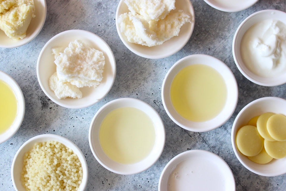 Natural skincare oils, butters and beeswax in white bowls.