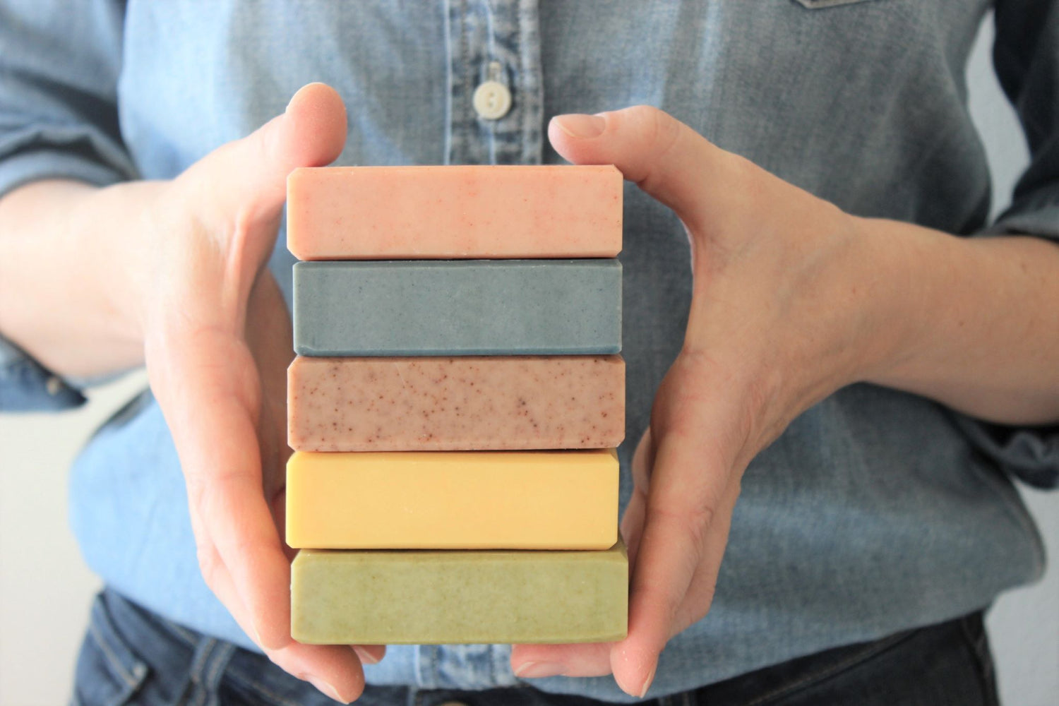 Woman holding five bars of natural, handcrafted soap in various colors.