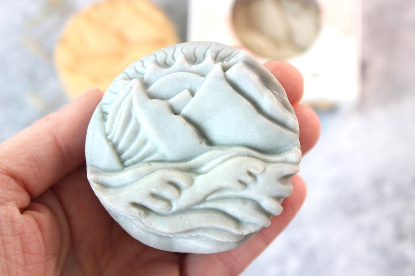 Alaskan Seaside soap, shaped as mountains.  Soap is blue and held in a hand.