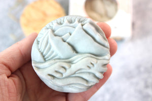 Alaskan Seaside soap, shaped as mountains.  Soap is blue and held in a hand.