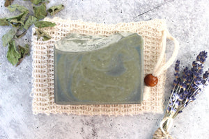 Alpine rainstorm soap on a cambric soap saver bag, next to dried lavender and peppermint leaves.