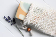 Load image into Gallery viewer, Cambric soap saver pouch with green, orange and white soap slipping out of bag.  Dried lavender in background.
