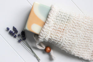 Cambric soap saver pouch with green, orange and white soap slipping out of bag.  Dried lavender in background.