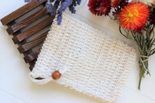Load image into Gallery viewer, A cambric soap saver bag is next to a bamboo soap dish.  Dried flowers in orange and purple are in the background.
