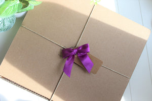 A recyclable gift box is wrapped with twine and a royal purple bow. Better For You Bars gift box.