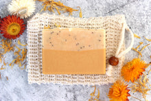 Load image into Gallery viewer, Lemon goat milk soap on a cambric soap saver pouch.  Dried yellow flowers in background.
