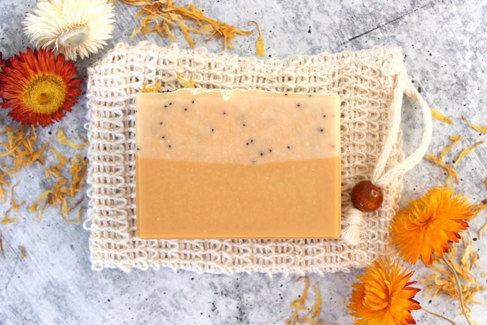 Lemon goat milk soap on a cambric soap saver pouch.  Dried yellow flowers in background.